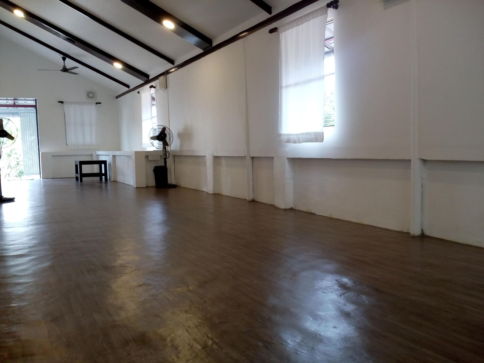 The practice hall at VHG Thiruvananthapuram, a beamed room with a wooden floor and curtained windows